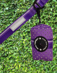 NeoCool™ Sport Poop Bag Holder in Purple with black logo dispenser attached to a leash against a green hedge background