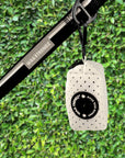 NeoCool™ Sport Poop Bag Holder in White with black logo dispenser attached to a leash against a green hedge background