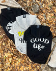 Hooded Sweatshirt For Dogs - "Good Life", "Bee Kind", and "Road Trip" hooded sweatshirts in black and gray - back view - outdoors laying on a log in a scenic fall background with brown leaves - Wag Trendz