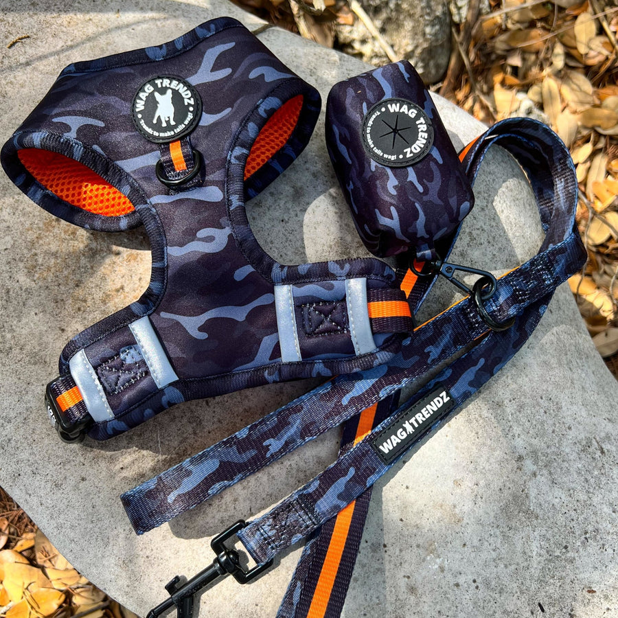 Dog Harness Vest - black and gray camo with orange accents on dog adjustable harness vest with front clip - chest side view - matching dog leash and poop bag holder - laying outdoors in the sun on a rock  - Wag Trendz
