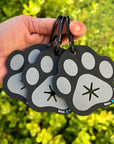 Poop Buddy - black and gray resin dog paw - set of 3 held by a hand - outdoors with greenery in the background - Wag Trendz