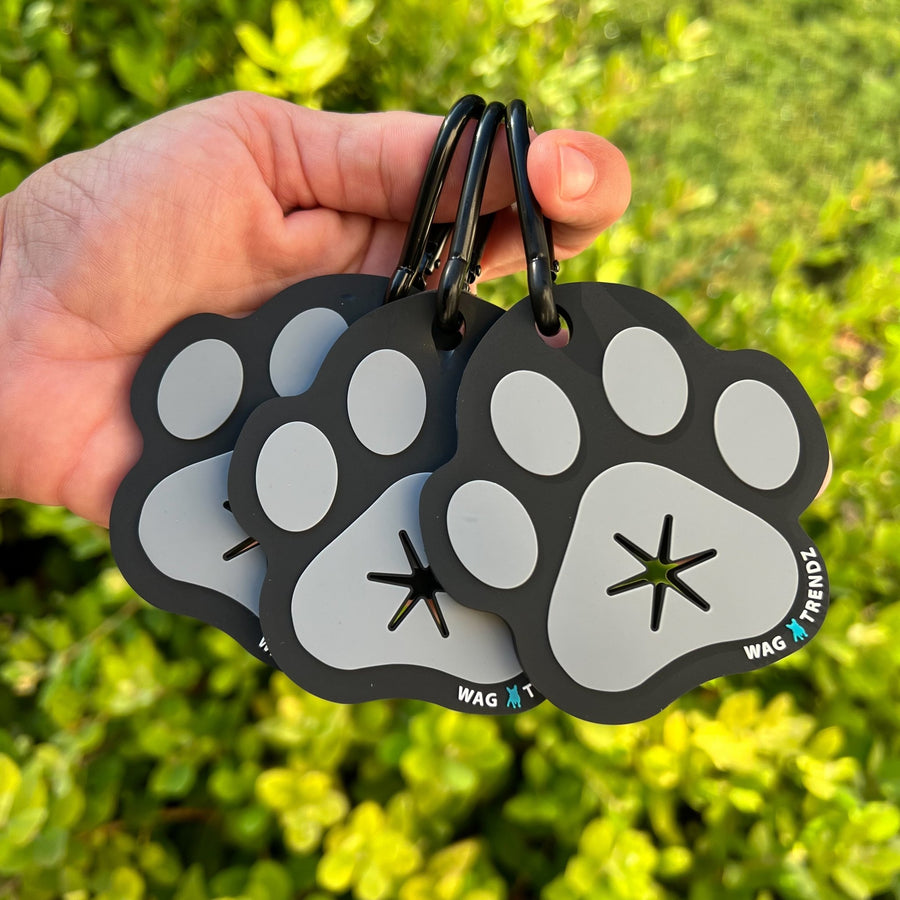 Poop Buddy - black and gray resin dog paw - set of 3 held by a hand - outdoors with greenery in the background - Wag Trendz 