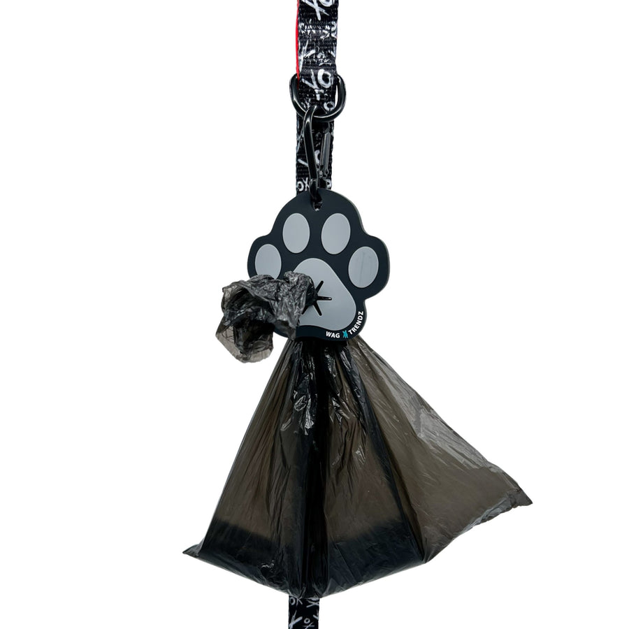 Poop Buddy - black and gray resin dog paw - hanging on a black & white XO dog leash with red accents and black plastic bag carrying poop pushed through hole - against white background - Wag Trendz